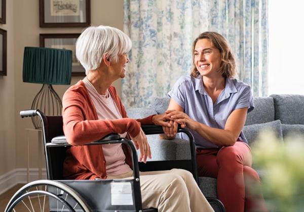 Mature woman comforting senior lady in wheelchair at nursing home.